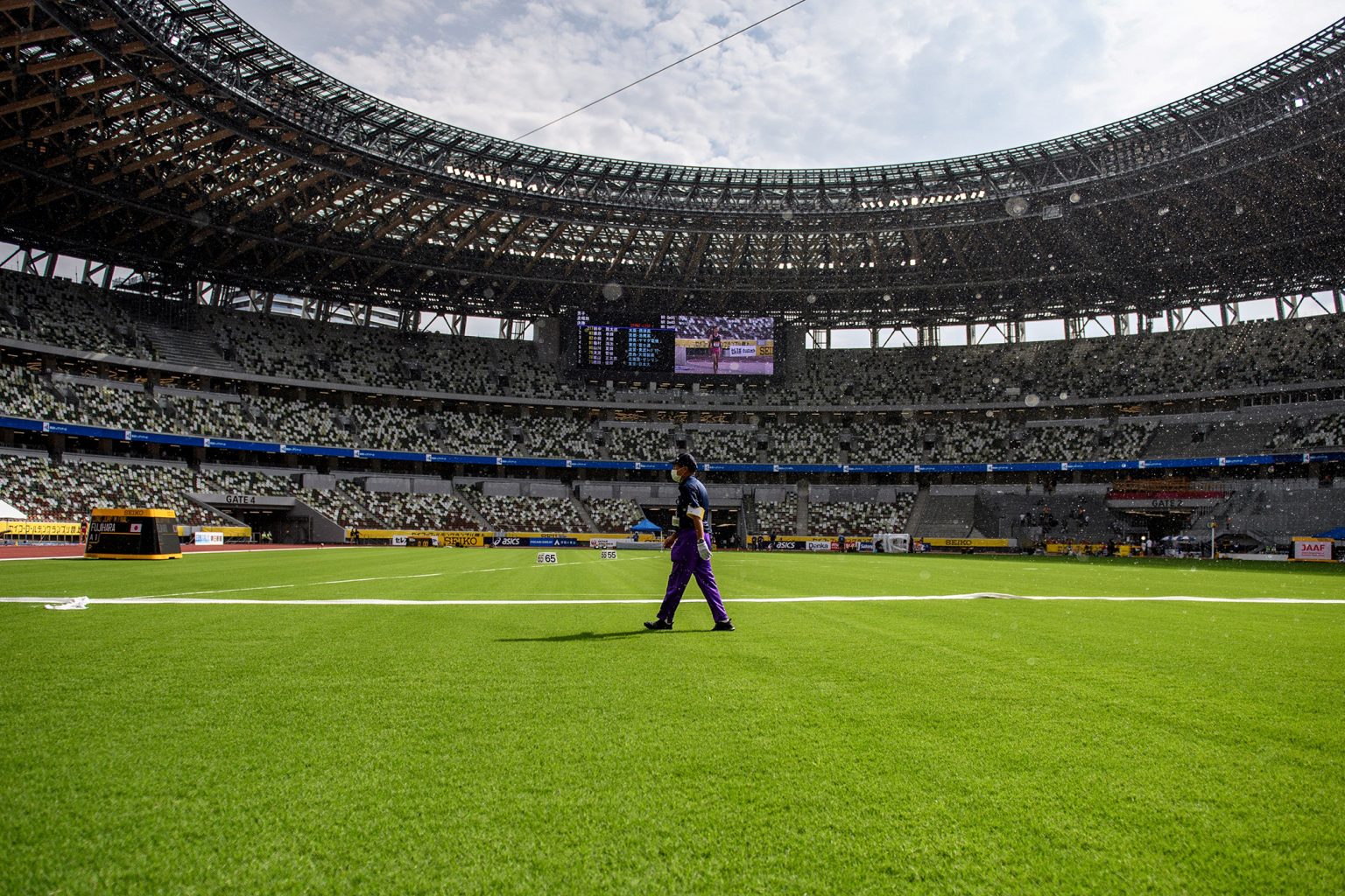 An official walks across the infield of the National Stadium in Tokyo, home of the 2020 Olympic Games. A UGA-bred grass will be used on the field. (Photo by PHILIP FONG/AFP via Getty Images)