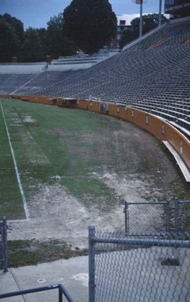 Sports stadium with areas of gray compacted soil with no grass