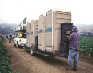 Photo showing portable toilet units with a worker using a handwashing station in a field 