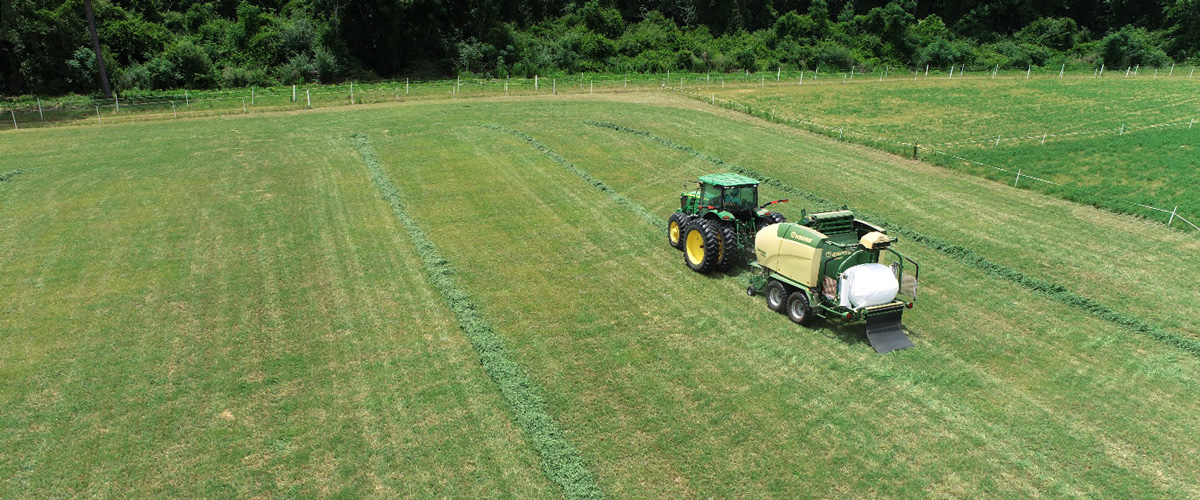 A tractor is seen from an overhead view in a field with bales of baleage visible.