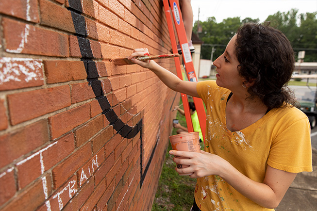 Woman painting on brick wall