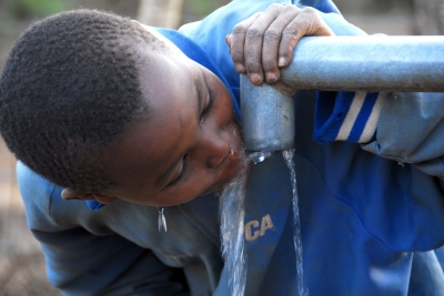 Photo of a child drinking water from an outdoor spigot