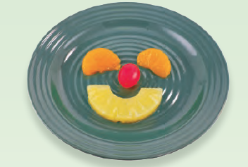 pineapple, cherry, and mandarin oranges arranged on a plate to look like a smiley face