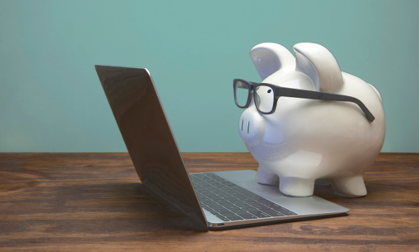 Piggy bank wearing glasses looking at a laptop