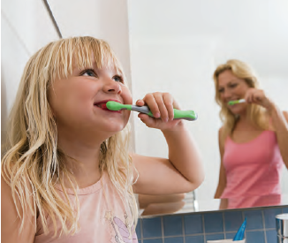 Child brushing teeth in front of her mom, also brushing her teeth