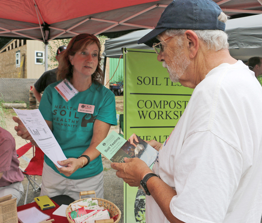 Two people under a tent at a farmers market discuss soil testing
