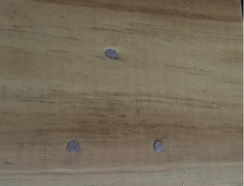 Wooden plank with three nails in it