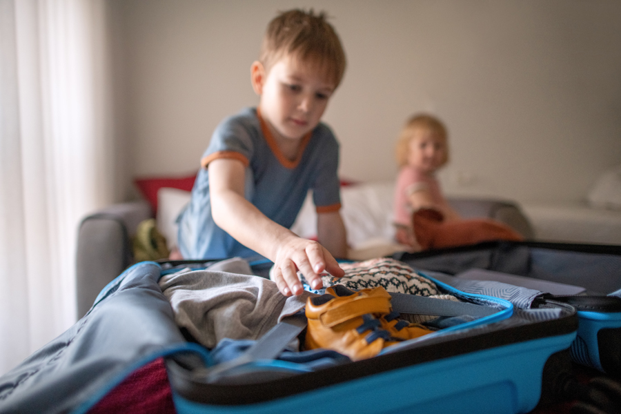 Two young children are on a bed packing a suitcase with their clothes