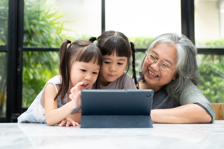 two young girls sit with an older woman and appear to be on a video call on an iPad or other tablet device