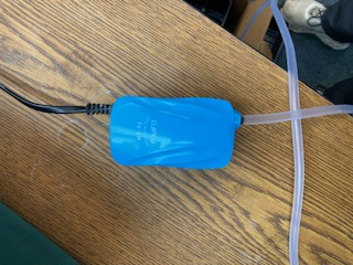 A bright blue plastic encased device is shown with an attached power line and an aeration tube