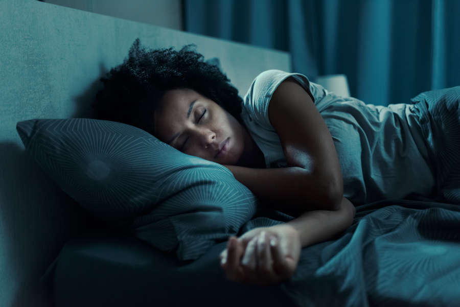 A woman sleeps in a bed in a darkened room.