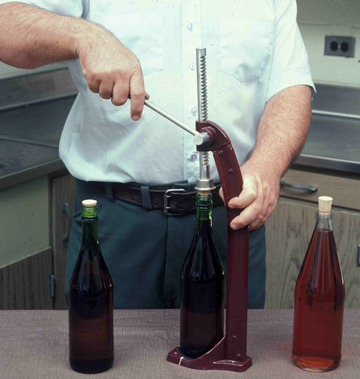 Glass bottles of wine being corked with a corking machine