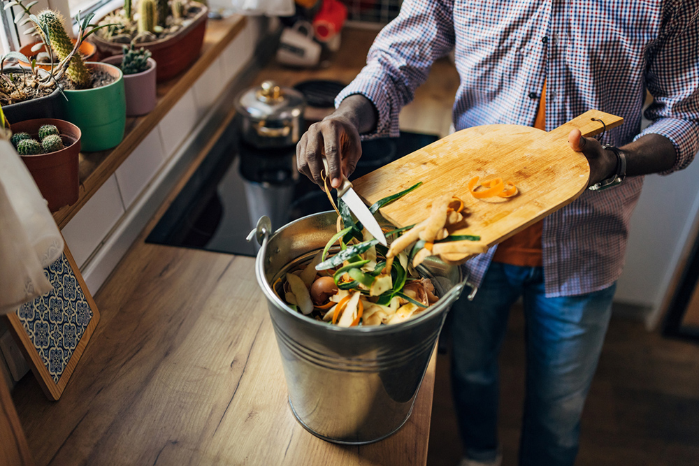 iStock image - a close up of hands scraping food from a cutting board into a compost bin.