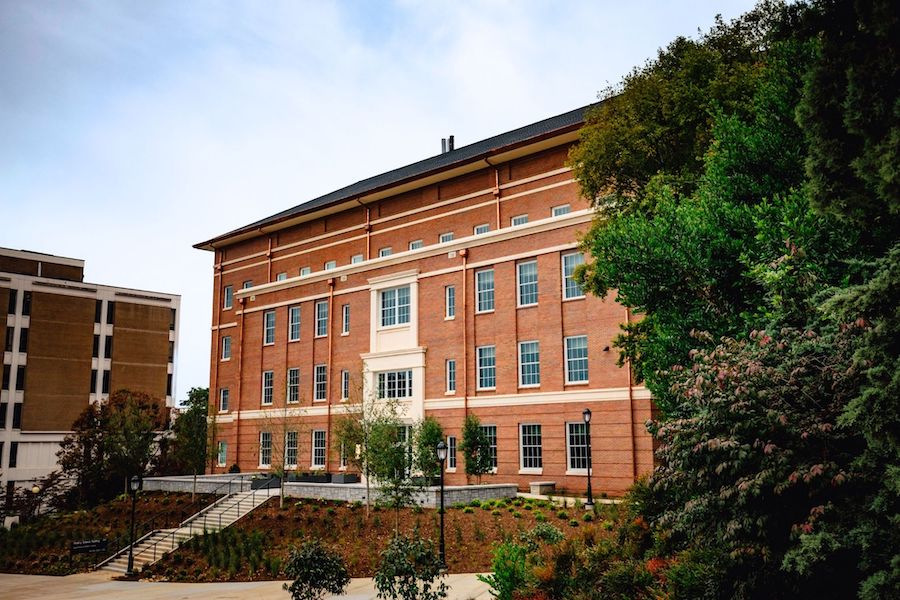 A large, four-story brick building sits center frame with trees in the foreground.