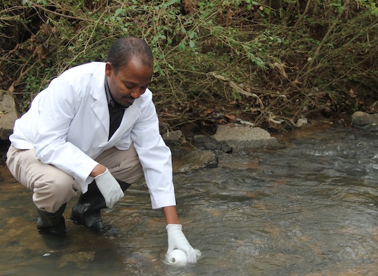 University of Georgia soil microbiologist Mussie Habteselassie takes a water sample from a stream on the UGA campus in Griffin, Ga.
