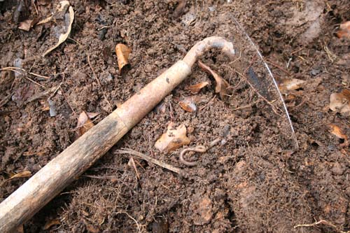 Soil covered spade laying in compost pile