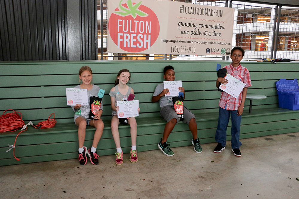 An exhausted but triumphant team of school-aged chefs — including Victoria Sweeney, 10, of Warren T. Jackson Elementary School; Parker Payne, 10, of Woodward Academy; Nile Smith, 10, of Roswell North Elementary School; and Isaiah Farrow, 10, of Georgia Connections Academy — celebrate after winning the inaugural Fulton Fresh Kids Cooking Competition on June 6 at the Ponce City Market Farmers Market.