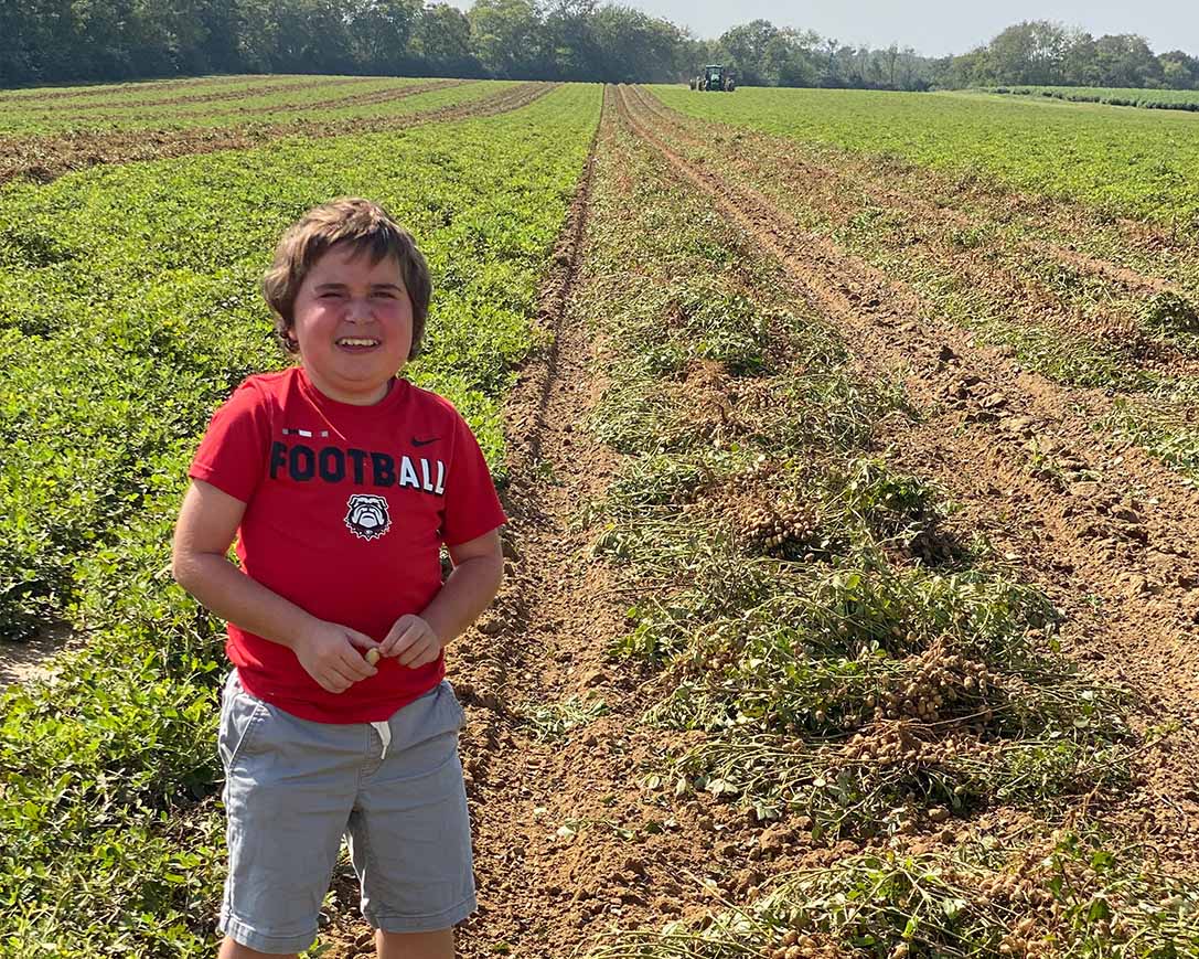 Wesley Cleveland poses for a photo in his favorite t-shirt, standing between rows of peanut crops during harvest.