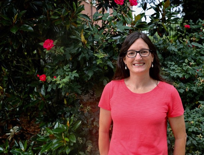 Professor Marin Brewer smiles in front of a flowering shrub on campus