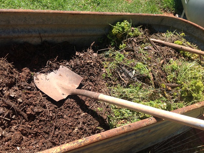 Shovel in compost bin with a lot of green material on one side