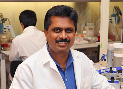 Anumantha Kanthasamy smiles in a lab wearing a blue collared shirt and white lab coat