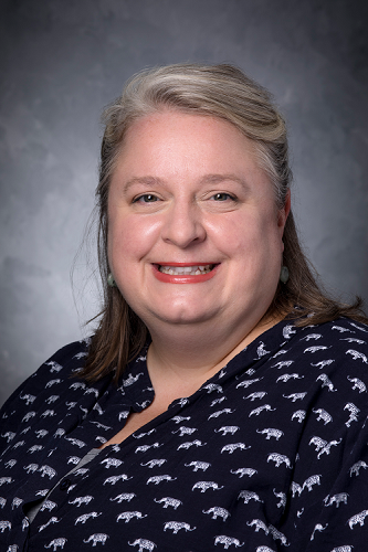 Faith Critzer, wearing a dark, elephant-print blouse, smiles in her professional headshot