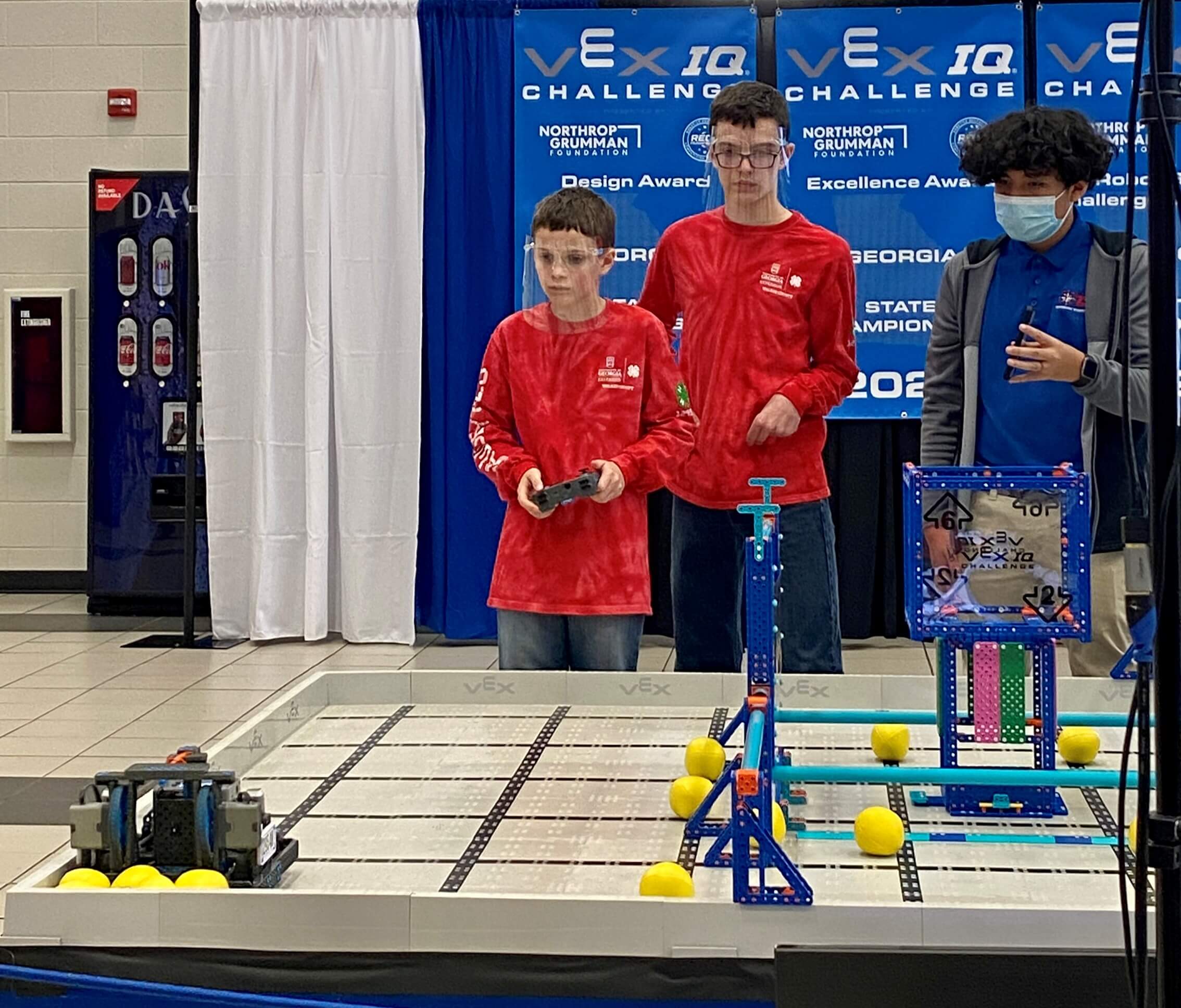 Members of the Dawgbytes team participate in a challenge at the Georgia VEX IQ Challenge Robotics competition while another participant looks on.