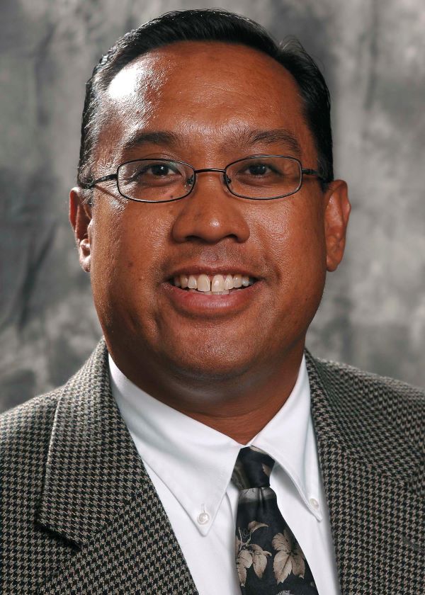John Salazar smiles in front of a gray background in his professional headshot