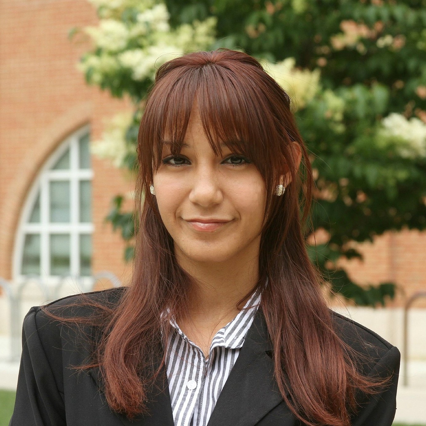 Kella Acevedo Villanueva smiles in front of a tree and building on campus