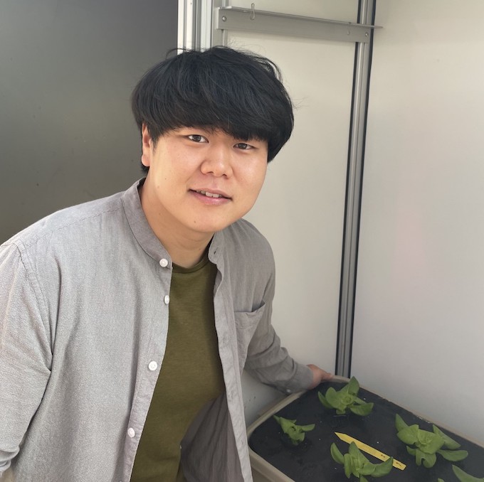 Changhyeon Kim smiles with his plants in a lab