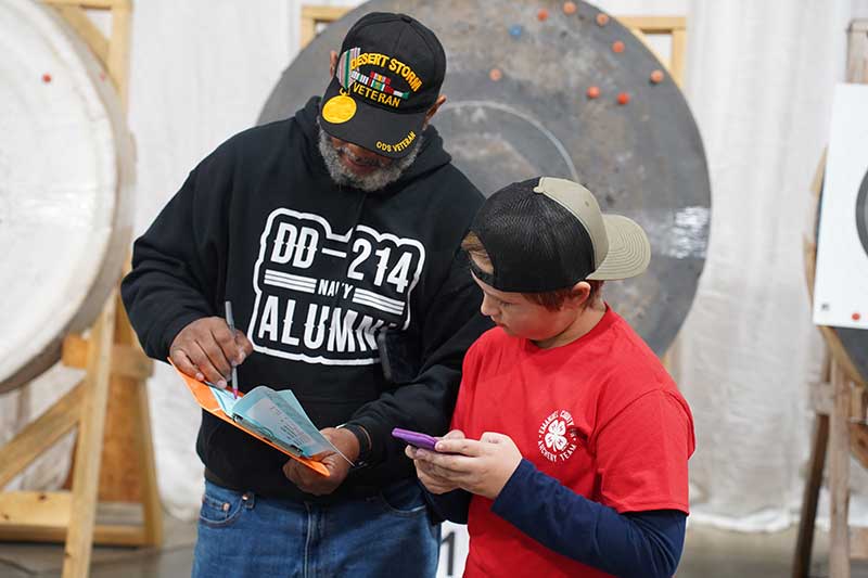 A Georgia 4-H SAFE volunteer helps an Emanuel County 4-H’er with his scores during an indoor archery match in Perry, Georgia.