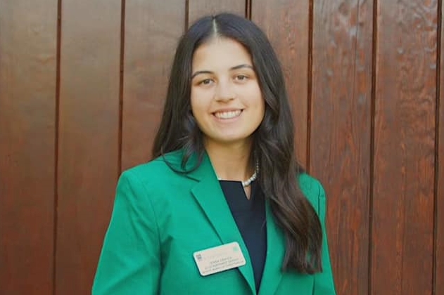 Jenna Dekich, a Catoosa County 4-H'er, smiles in front of a wood-paneled wall while wearing a green blazer