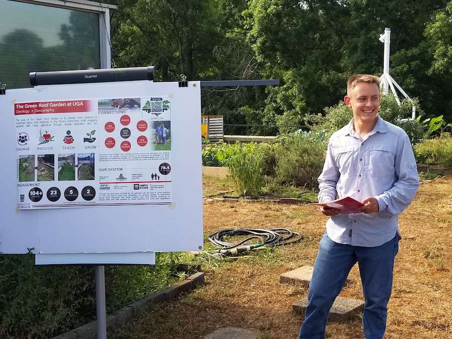 UGA graduate student and green roof manager Andrew MacElroy answers questions while standing next to his poster presentation on the rooftop garden