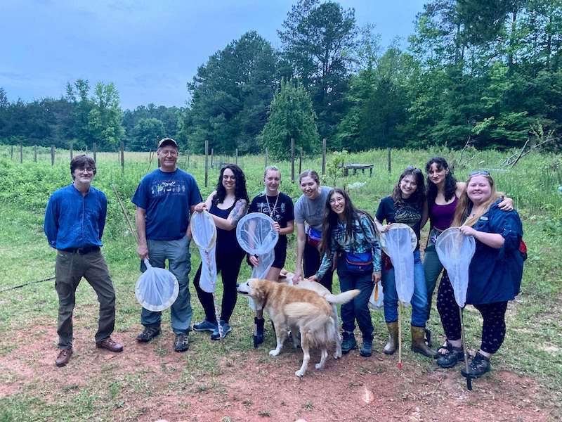 The firefly expedition group gathers on the property while carrying insect collection nets and petting two yellow dogs