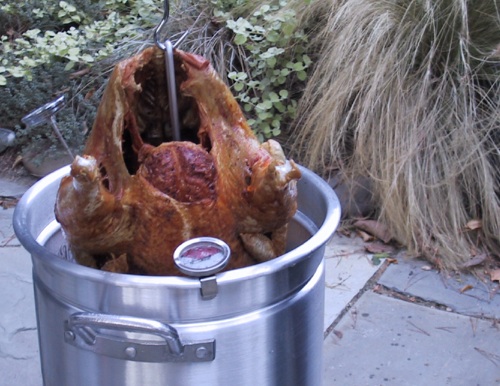 A fried turkey is lifted from a pot of hot oil