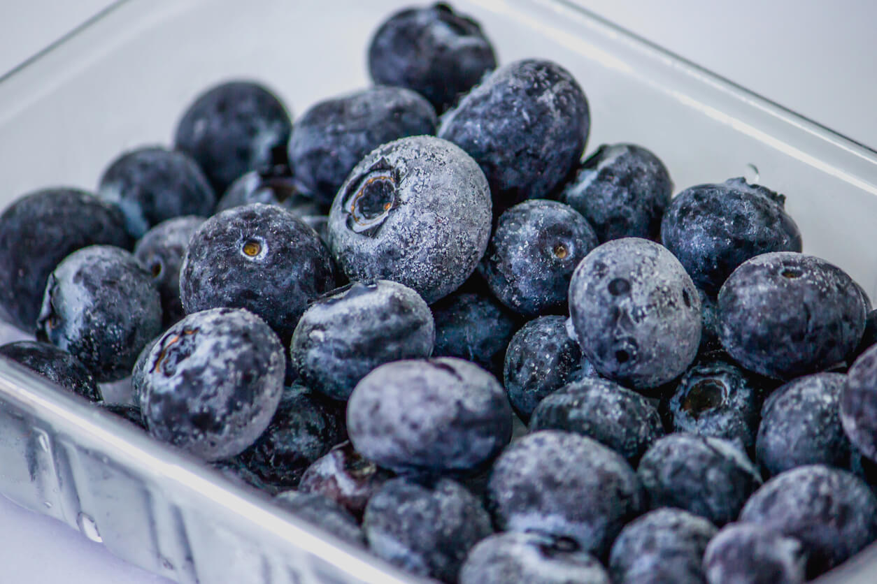 Close-up of a clear glass container full of frozen blueberries on a white surface