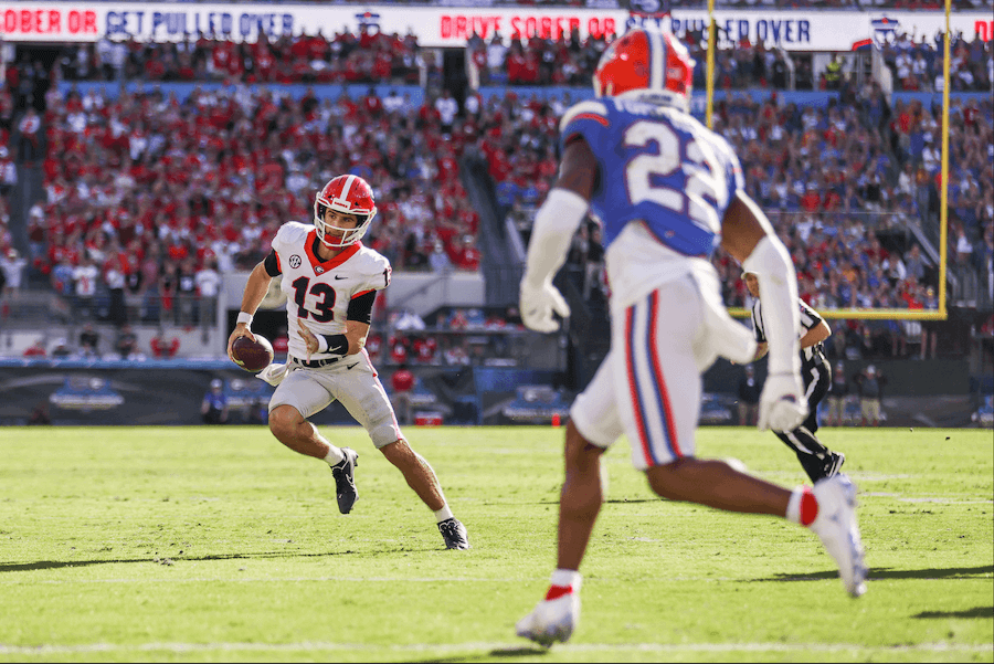 Stetson Bennett, UGA quarterback wearing the No. 13, faces off with a UF player during the UGA vs. UF football game in Jacksonville in October 2021. The stands in the background are full and a banner reads "Drive sober or get pulled over."