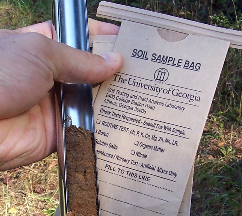 A small, brown UGA soil sample bag and metal probe full of soil
