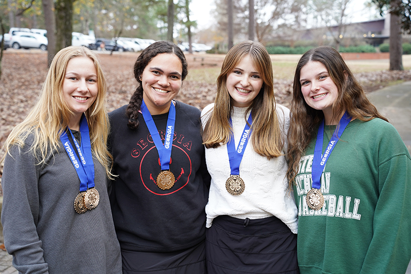 Oconee County 4-H senior Consumer Judging Team members Lexi Pritchard, Alyssa Haag, Robie Lucas and Lilly Ann Smith stand side by side, smiling and wearing their team and individual medals around their necks. 