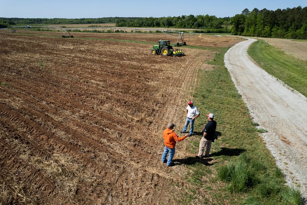 (Foreground L-R): Farm manager Josh Griffin, assistant professor and extension precision ag specialist Simer Virk and agriculture specialist Kevin Roach talk as a tractor operator plants corn using a precision agriculture system at the Iron Horse Farm. (Photo by Andrew Davis Tucker)