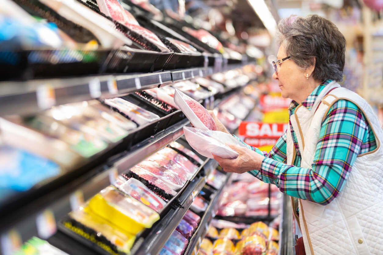 An older consumer compares prices in the meat aisle of the grocery store