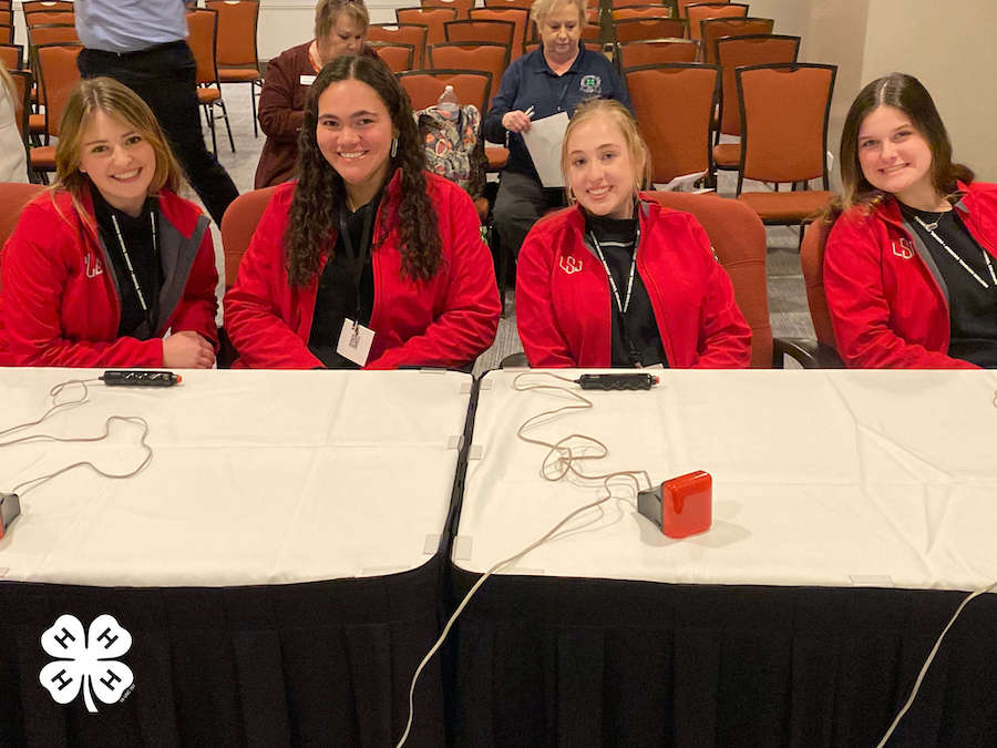 Wearing matching red jackets and black shirts, four Oconee County 4-H'ers compete at a table with buzzers at the Western National Roundup event in Denver.