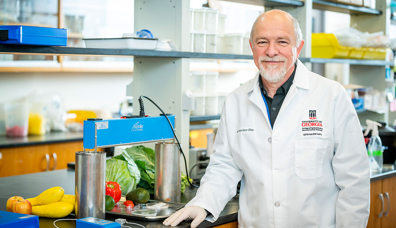 Francisco Diez wears a white lab coat while standing in his lab at the UGA Center for Food Safety