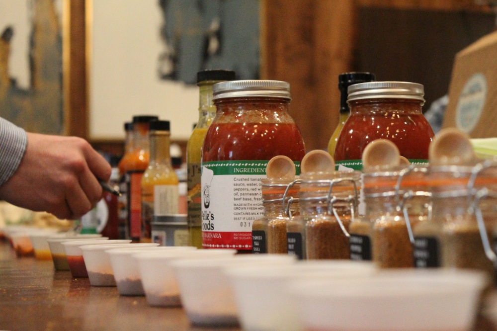 A Flavor of Georgia judge holding a pen tastes a variety of submitted sauces and seasonings, but only his hand and the product arrangement is visible