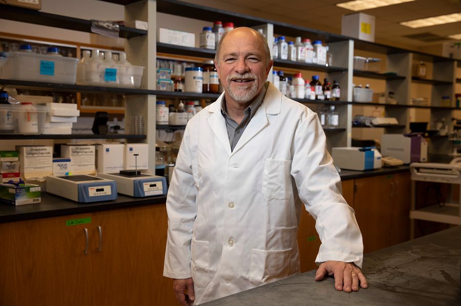 Francisco Diez, wearing a white lab coat, stands in his laboratory with his hand on the counter