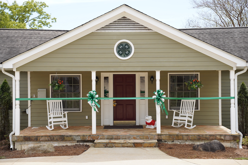 The administration building with a rocking chair front porch and Bulldog statue, tied off with a green ribbon for the ribbon-cutting ceremony