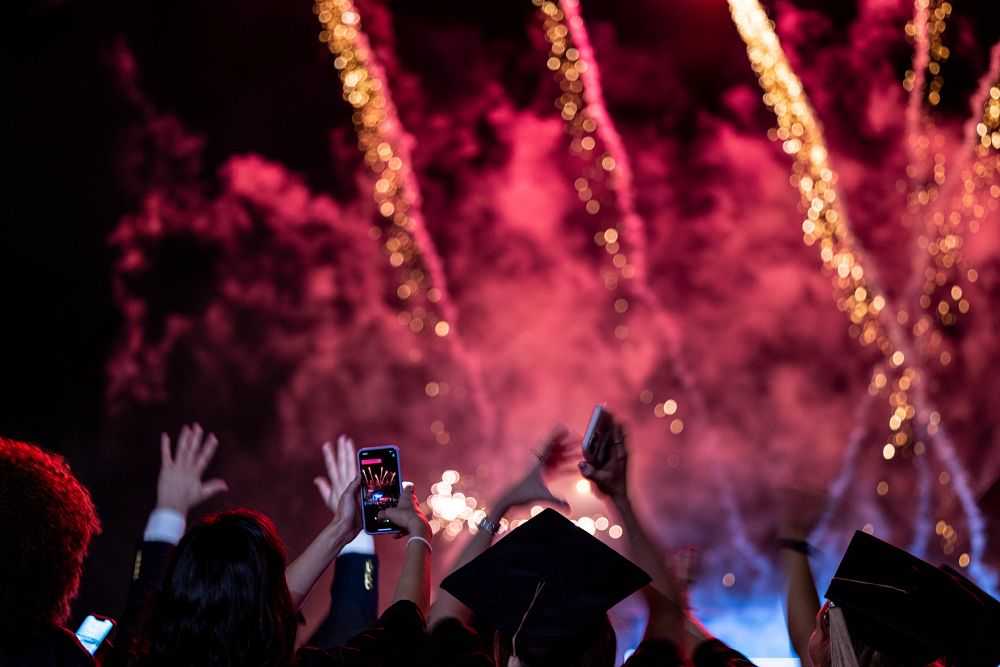 Detail of students raising their hands and taking photos during the fireworks celebration at then 2022 Spring Undergraduate Commencement in Sanford Stadium.