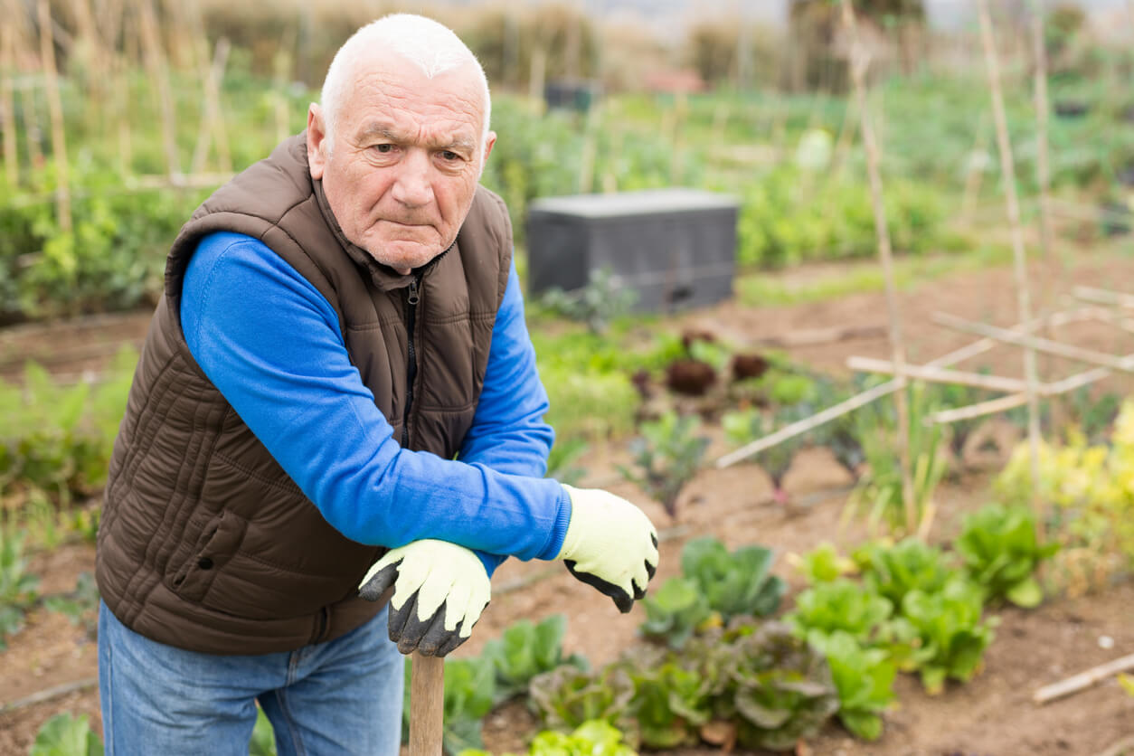 Senior farmer leans against garden tools looking worried