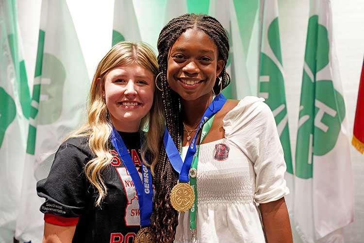 Georgia Master 4-H'ers Grace Holt from Toombs County and Sophia Melbourne from Cherokee County pose in front of 4-H flags.