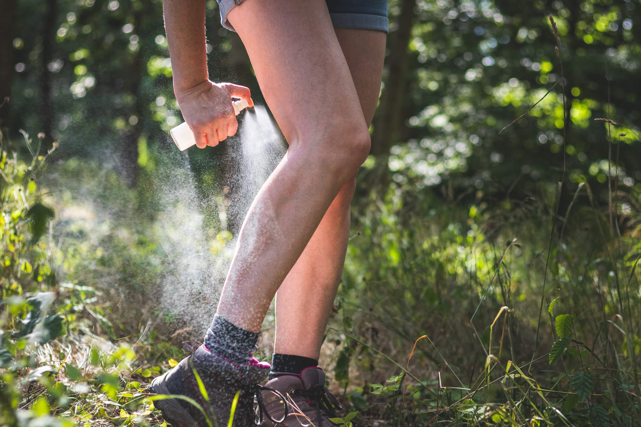 Woman applying mosquito repellent on her legs while hiking in a wooded area